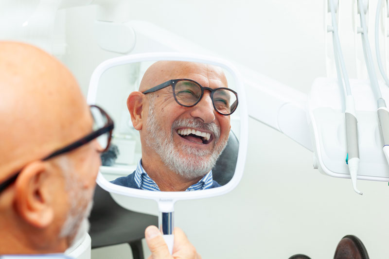 elderly man smiling in a dental office, looking through mirrior at teeth